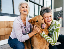 Two women pet a golden retriever.