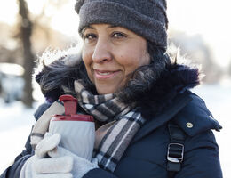 A woman dressed in winter gear holding a travel mug.