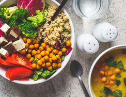 A bowl of soup next to a salad with chopped vegetables, tofu, chickpeas and quinoa.