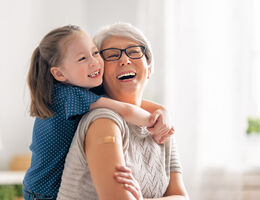 A girl hugs an older woman with a bandage on her upper arm.