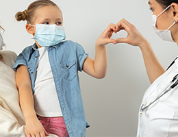 A child and a healthcare provider hold their hands together in the shape of a heart. 