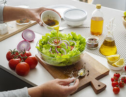 A hand pours a homemade vinaigrette onto a bowl of salad.