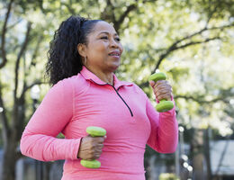 A woman in pink walks with a pair of hand weights.
