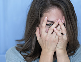 A woman covers her face with her hands. One eye shows through her fingers. 