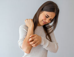 A woman scratches red spots on her forearm.