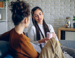Two women sit on a couch and talk.