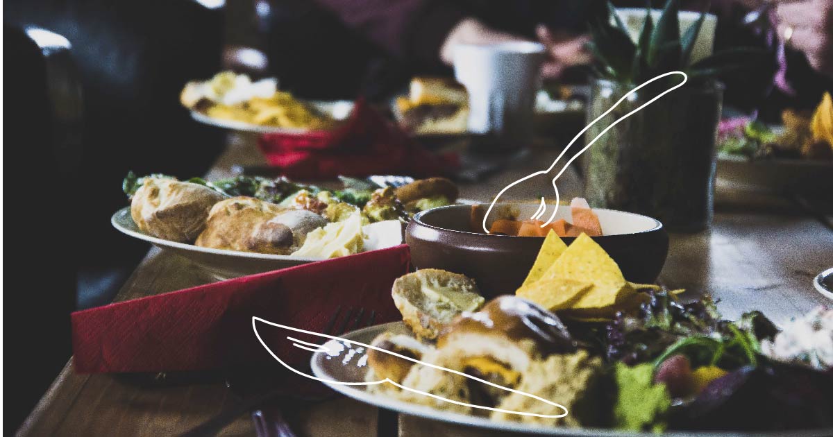 A table full of plates of food with whimsical utensils drawn in white.