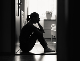 A woman silhouetted in a doorway, sitting on the floor with a hand to her eyes