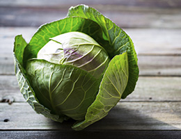 A head of cabbage sits on a rustic wooden table.