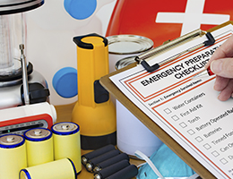 An emergency checklist on a clipboard with batteries, a radio, a flashlight and other supplies.